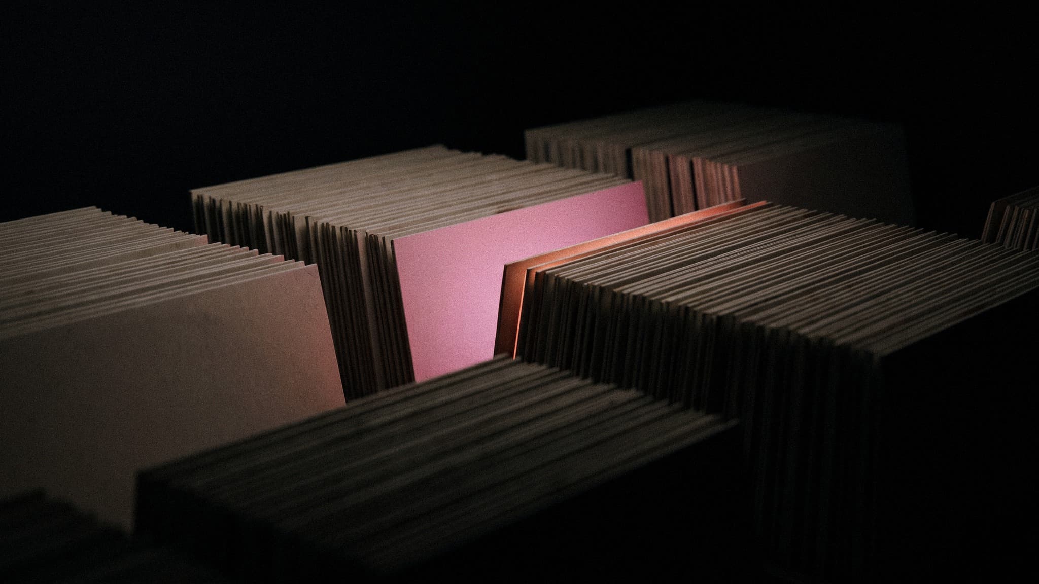 Rows of identical blank record sleeves receding into the dark, with one sleeve lit orchid pink among them