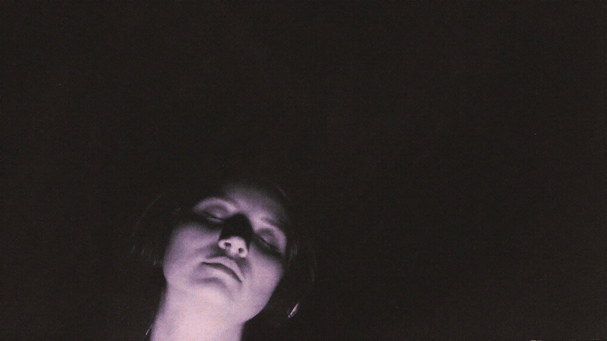 A listener with headphones, eyes closed, face lit by a faint violet glow